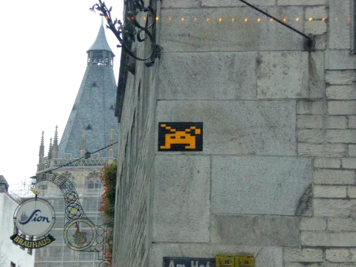 eine Straßenecke in Köln mit Straßenkunst und einem Sion-Kölsch-Schild.
