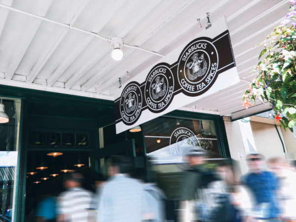 Unter dem Starbucks-Schil mit Original-Logo strömen Menschen in das Café